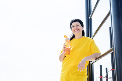 Portrait of smiling woman standing against yellow wall