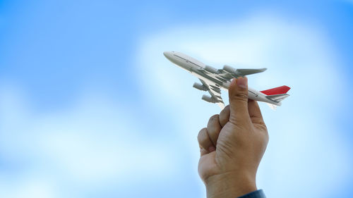 Low angle view of hand holding toy airplane against sky