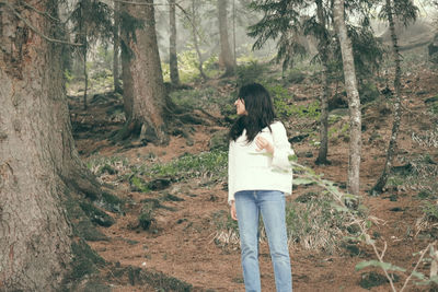 Rear view of woman standing by tree trunk in forest