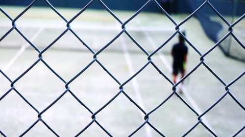 Defocused image of tennis player in court seen through chainlink fence