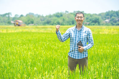 Portrait of smiling man on field holding digital tablet