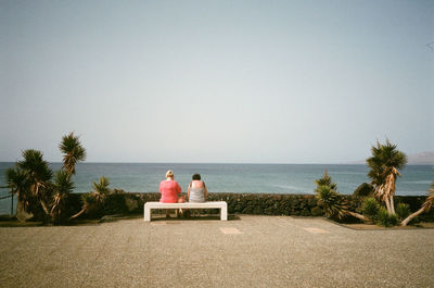 Women sitting at beach against clear sky