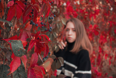 Autumn portrait of a beautiful cute woman against a background of bright red leaves. black sweater