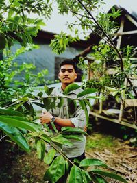 Portrait of young man with arms crossed standing by plants