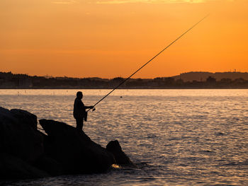 Silhouette man fishing in sea against sunset sky