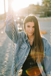 Portrait of smiling young woman holding chain at playground during sunset