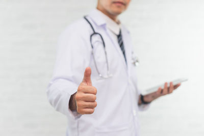 Midsection of doctor gesturing thumbs up