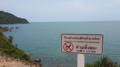 Information sign on cliff by sea against clear sky