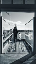 Rear view of man with daughter standing on glass floor by bridge at harbor