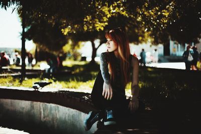 Young woman looking down while sitting on tree