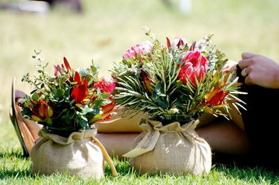 Low section of woman sitting by flower vase on grassy field