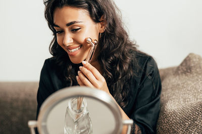 Smiling young woman using jade roller at home