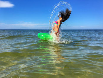 Playful girl tossing hair in sea against sky