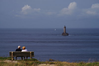 Rear view of man sitting by sea against sky