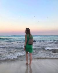 Full length of woman standing on beach against sky during sunset