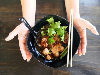 High angle view of two hand hold the black bowl of rice noodles soup with beef, meat ball