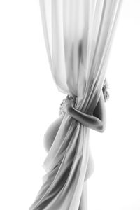 Side view of naked pregnant woman standing behind curtain against white background