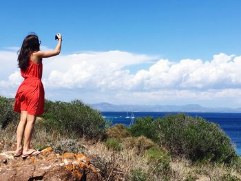 Rear view of woman standing on rock by sea against sky