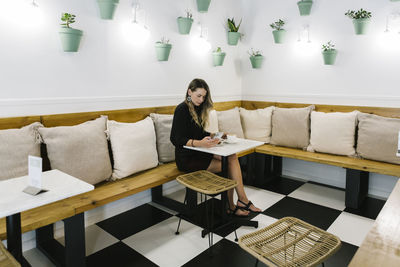 Mid adult woman using mobile phone while eating food at coffee shop