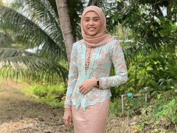 Portrait of smiling young woman in hijab standing against trees