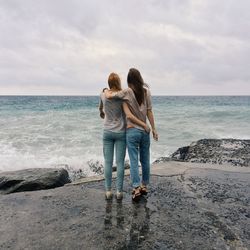 Full length rear view of friends standing on rock viewing sea