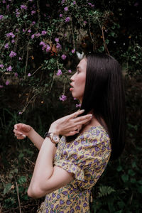 Side view of young woman standing by flowering plants