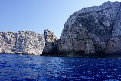 Rock formations in sea against clear blue sky