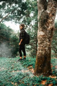 Full length of woman standing by tree trunk in forest