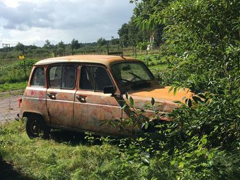 Abandoned car on field against sky