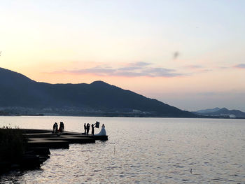 Silhouette people on lake against sky during sunset