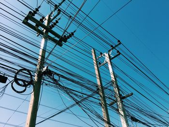 Low angle view of electricity pylons against clear blue sky