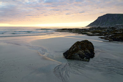 Scenic view of rocks on beach against sky during sunset