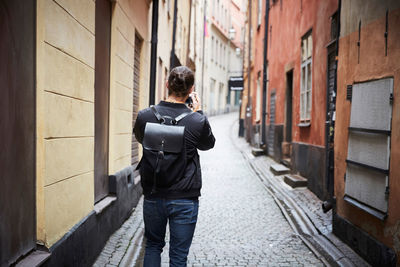 Rear view of man photographing through camera while standing on cobbled street in alley