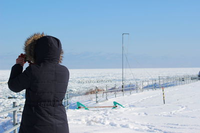 Rear view of woman standing by frozen sea