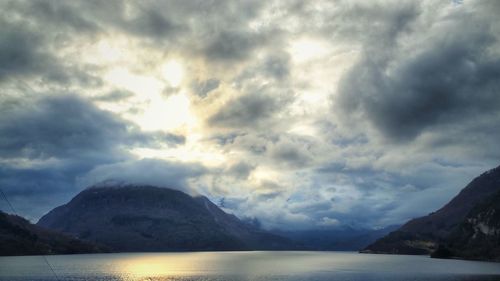 Scenic view of sea and mountains against storm clouds