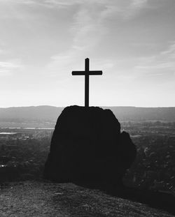 Statue of cross on landscape against sky