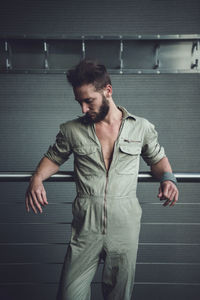 Thoughtful handsome mid adult man looking down standing by railing against wall