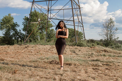 Full length portrait of young woman standing against sky