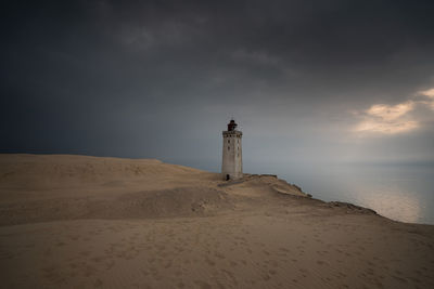 Lighthouse on beach by sea against sky