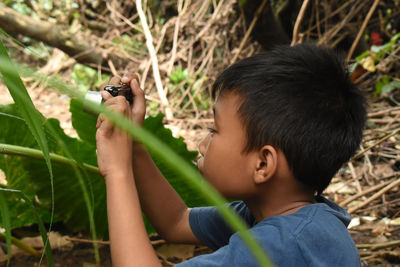 Side view of boy photographing plant in forest