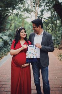 Couple holding baby clothing while standing outdoors