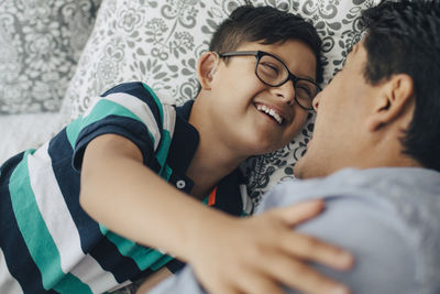 Happy disabled boy looking at father while lying on bed at home