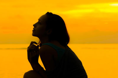 Side view of woman at beach against sky during sunset