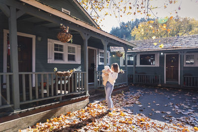 A woman with a child is standing near a house on yellow leaves