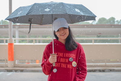 Young woman holding umbrella while standing on road during rainfall in city