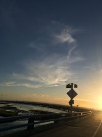 Road sign in city against sky during sunset