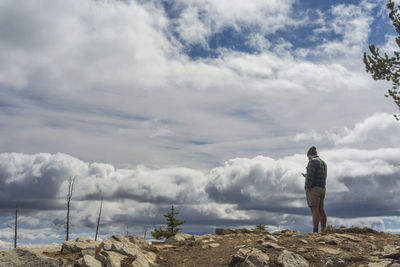 Male standing on mountain top looking at cell phone with moody clouds