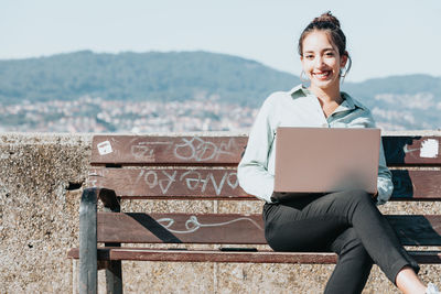 Young woman using laptop while sitting on bench