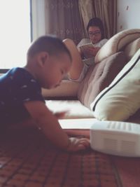 Boy by sofa with sister using digital tablet in living room at home