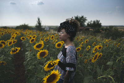Side view of woman standing amidst sunflowers on field against sky